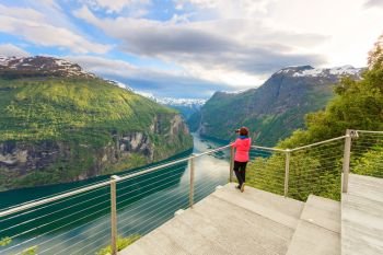 Tourism vacation and travel. Female tourist enjoying beautiful view over magical Geirangerfjorden from Flydalsjuvet viewpoint, taking photo with camera, Norway Scandinavia.. Tourist taking photo from Flydasjuvet viewpoint Norway