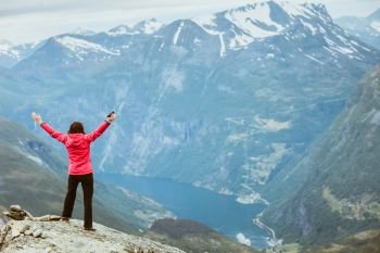 Tourism vacation and travel. Happy free tourist woman with arms raised outstretched up looking at Geirangerfjord and mountains landscape from Dalsnibba viewpoint, Norway Scandinavia.. Tourist woman on Dalsnibba viewpoint Norway