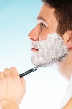 Young man shaving using razor with cream foam. Handsome guy removing face beard hair. Skin care and hygiene.. Young man shaving using razor with cream foam.