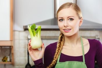 Woman in kitchen holding green fresh raw fennel bulb vegetable. Young housewife cooking. Healthy eating, vegetarian food, dieting and people concept.. Woman in kitchen holds raw fennel bulb vegetable