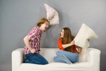 Happy funny siblings couple having pillow fight for fun. Enjoying leisure time with friends at home.. Man and woman having pillow fight