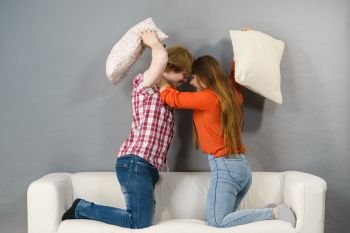 Angry couple having pillow fight. Brother and sister having conflist on sofa.. Angry couple having pillow fight