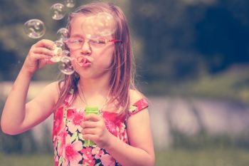 Little girl child blowing soap bubbles outdoor. Kid having fun in park. Happy and carefree childhood. Instagram filtered.. Little girl child blowing soap bubbles outdoor.