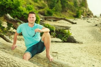 Summertime relaxation, vacation and holiday, adventure traveling concept. Handsome man sitting on tree trunk relaxing during summer.. Handsome man relaxing on beach during summer.