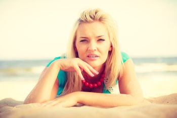 Portrait of attractive blonde woman lying on sandy beach relaxing during summertime. Woman lying on sandy beach relaxing during summer