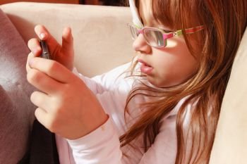 Childhood, childcare, being polite concept. Little toddler girl with bandage on eye playing games on smartphone. Toddler girl with bandage on eye playing games