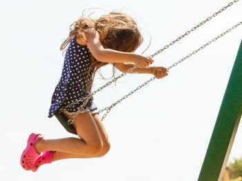 Have fun and leisure concept. Long haired enjoyable girl swinging outdoor in garden playground. Lovely child playing on swing-set.. Girl swinging on swing-set.