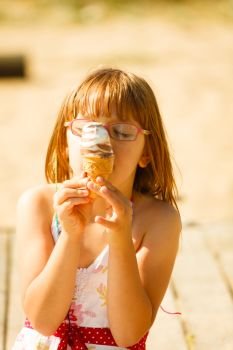 Summertime joy, summer recreation outside concept. Toddler girl in eyeglasses eating ice cream on beach. Toddler girl eating ice cream on beach