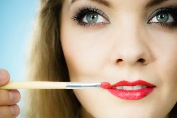 Professional make up artist applying on woman fashion model lips red lip gloss or lipstick using brush. Visage last touch concept.. Applying lipstick on fashion model lips