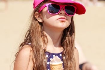 Kid eating gelato soft serve ice cream on beach. Little girl in sunglasses enjoying summer holidays vacation outdoor.. Little girl kid eating ice cream on beach. Summer.