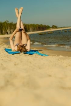 Summertime pleasures, enjoying vacation concept. Woman in bikini sunbathing and relaxing on beach, using smartphone checking social media and writing sms. Woman in bikini sunbathing and relaxing on beach