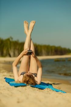 Summertime pleasures, enjoying vacation concept. Woman in bikini sunbathing and relaxing on beach, using smartphone checking social media and writing sms. Woman in bikini sunbathing and relaxing on beach