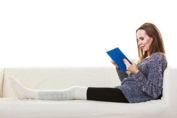 Leisure, education, literature and home concept. Woman sitting on couch reading book at home