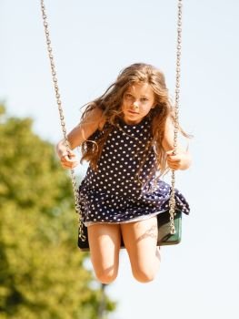 Have fun and leisure concept. Long haired enjoyable girl swinging outdoor in garden playground. Lovely child playing on swing-set.. Girl swinging on swing-set.