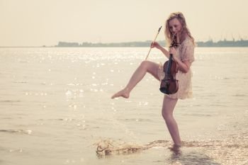 Music love, hobby and everyday passion concept. Woman on beach near sea holding violin playing in water. Woman on beach near sea holding violin