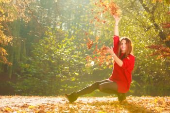 Autumn time. Fun and carefree. Cheerful lovely young woman playing with leaves. Girl relax in autumnal park forest surrounded by trees with flying leaf.. Playful woman outdoors playing with leaves.
