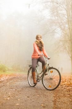 Happy active woman riding bike bicycle in foggy fall autumn park. Glad young girl in sweater and earmuffs relaxing. Healthy lifestyle and recreation leisure activity.. Happy active woman riding bike in autumn park.