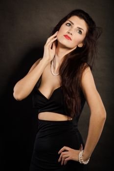 Party celebration concept.  Magnificent long hair woman red lipstick wearing black evening dress pearls necklace on dark. woman in sensual black dress on dark