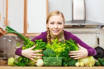 Woman young positive housewife in kitchen with many green leafy vegetables, fresh produce organically grown on counter. Healthy lifestyle, cooking, vegetarian food, dieting and people concept.. Smiling woman in kitchen with green vegetables