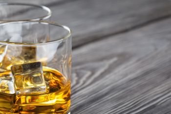 Fragment of two glasses of whiskey with ice on wooden background blurred. Fragment of two glasses of whiskey with ice