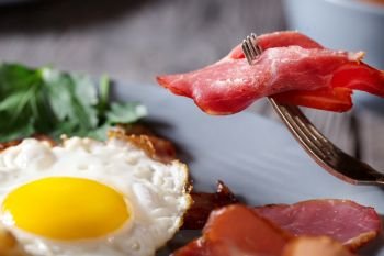 Fragment of appetizing bacon on a fork and fried eggs. The concept of healthy, natural nutrition. Close-up.. Fragment of appetizing bacon on a fork and fried eggs