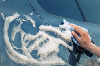 Car washing with a blue sponge. Female hand washes the machine with soap foam. Toning. Car washing with a blue sponge