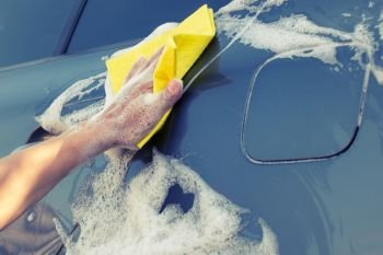 Car washing with a yellow sponge. Female hand washes the machine with soap foam. Car washing with a yellow sponge
