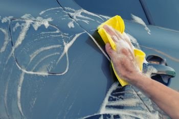 A female hand with a yellow sponge in a soapy foam washes the car. Female hand with yellow sponge in soapy foam washes the car