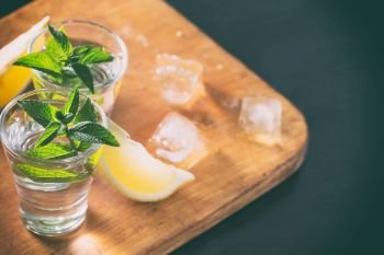 Two glasses of gin or vodka with mint and lemon with ice on a wooden background. Alcoholic cocktail. Copy the space. Two glasses of gin or vodka with mint and lemon with ice