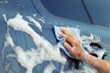 Woman’s hand with a blue sponge in a soapy foam washes the car