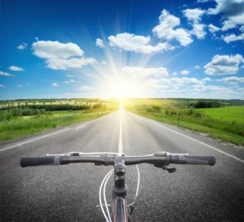 Bicycle handlebar on the background of an asphalt road to the bright sun. Collage. Bicycle handlebar on the background of road to bright sun