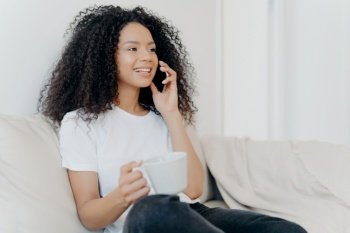 Smiling woman chatting on the phone and holding a mug, enjoying a relaxed moment at home