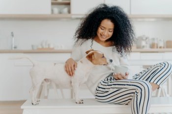 Woman with curly hair enjoys a quiet moment with her dog, a cozy scene with a warm drink