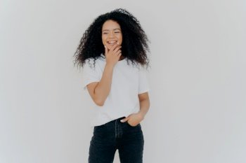 Laughing young woman in a casual white tee and jeans, hand on chin, with a joyful expression