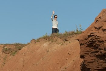 Woman waving from top of rocky cliff, Green Gables, Cavendish, Prince Edward Island, Canada