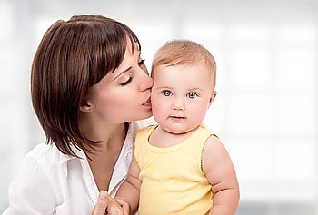 Portrait of beautiful mother with pleasure kissing her cute adorable little daughter at home, happy young family, love and happiness concept