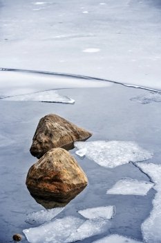 Icy shore in winter. Broken ice floating on water at cold lake shore with rocks in winter