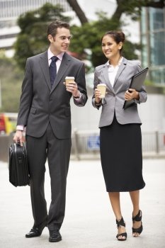 Businessman And Businesswoman Walking Along Street Holding Takeaway Coffee