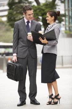 Businessman And Businesswoman Discussing Document In Street Holding Takeaway Coffee