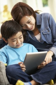 Chinese Mother And Son Using Tablet Computer Whilst Sitting On Sofa At Home