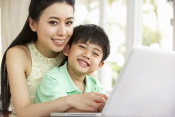 Chinese Mother And Son Sitting At Desk Using Laptop At Home
