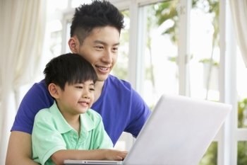 Chinese Father And Son Sitting At Desk Using Laptop At Home