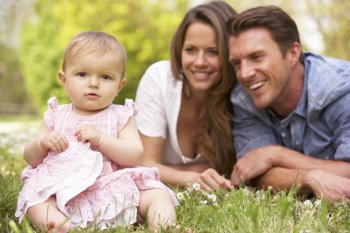 Parents With Baby Girl Sitting In Field Of Summer Flowers