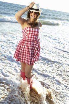 Teenage Girl Wearing Wellington Boots Splashing In Sea On Beach Holiday