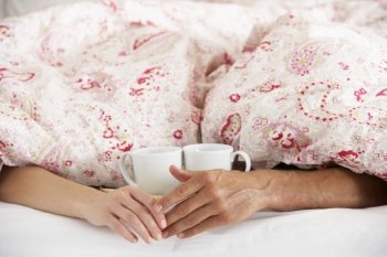 Romantic Couple Holding Hands Under Duvet In Bed