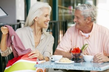 Senior Couple Enjoying Snack At Outdoor Cafe After Shopping