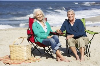 Senior Couple Sitting On Beach In Deckchairs Having Picnic
