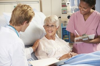Doctor With Nurse Talking To Senior Female Patient In Bed