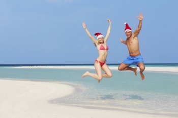 Couple Jumping On Beach Wearing Santa Hats