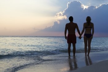 Silhouette Of Couple Walking Along Beach At Sunset